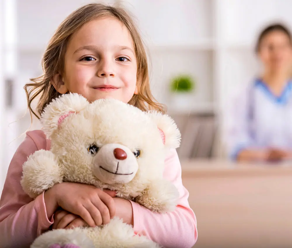 A young girl holds a teddy bear in the hospital.
